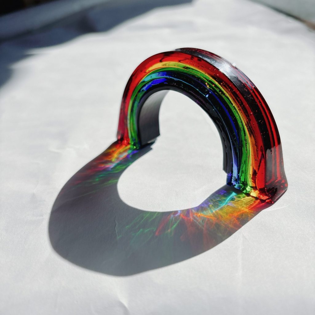 窓辺に飾られたガラス製の虹のオブジェ。光を受けて虹色の影が差し込むインテリア雑貨。