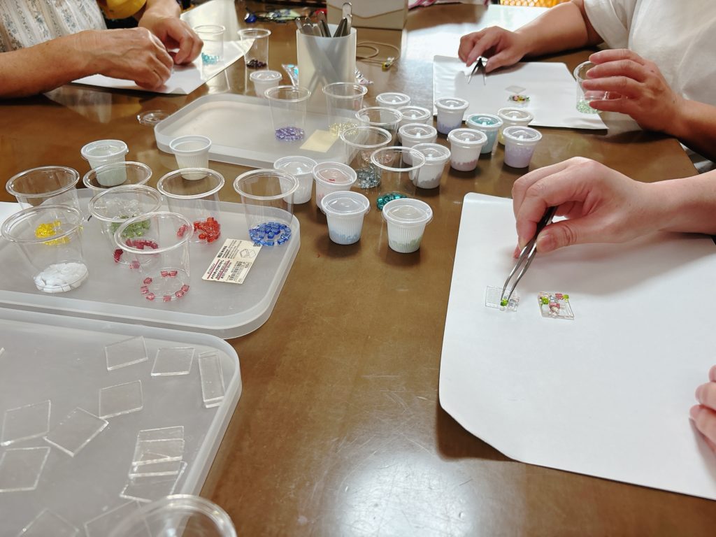 参加者がネックレス作りに集中しているガラスアートワークショップの風景。