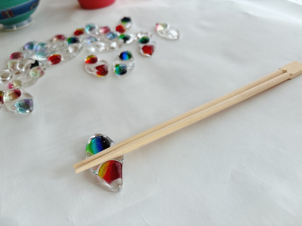 割り箸が、2粒の枝豆を模したガラス製の箸置きに乗せられている様子。箸置きの丸みと透明感が引き立っている。