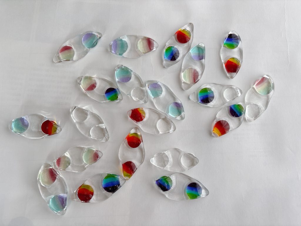 白い背景の上に、カラフルな豆が二粒ずつ入ったガラスの箸置きが整然と並べられている。透明感と光沢が美しい。