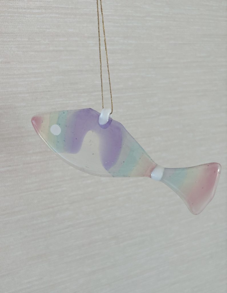 吊り下げられたパステルマーブル模様のガラスの魚オブジェ。柔らかい色合いが特徴のインテリア向け作品。