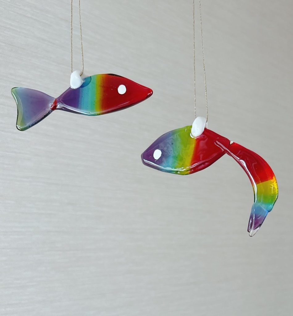 虹色のグラデーションをまとったガラス製の魚型オーナメント。複数の虹魚が吊るされ、風に揺れる様子。