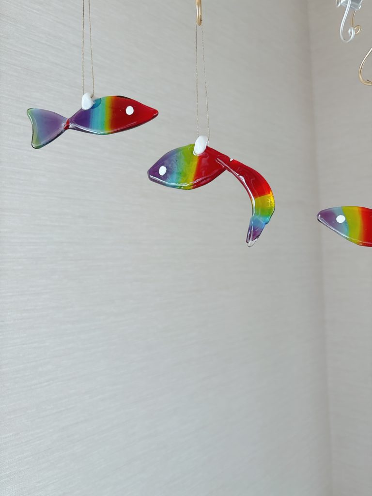 虹色のグラデーションを持つガラス作品「虹魚（にじうお）」。吊り下げタイプのインテリア雑貨で、光を受けて輝くハンドメイドの魚モチーフ。